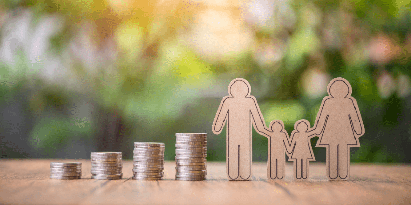 A stack of coins next to small cardboard figurines of 2 parents and 2 children.