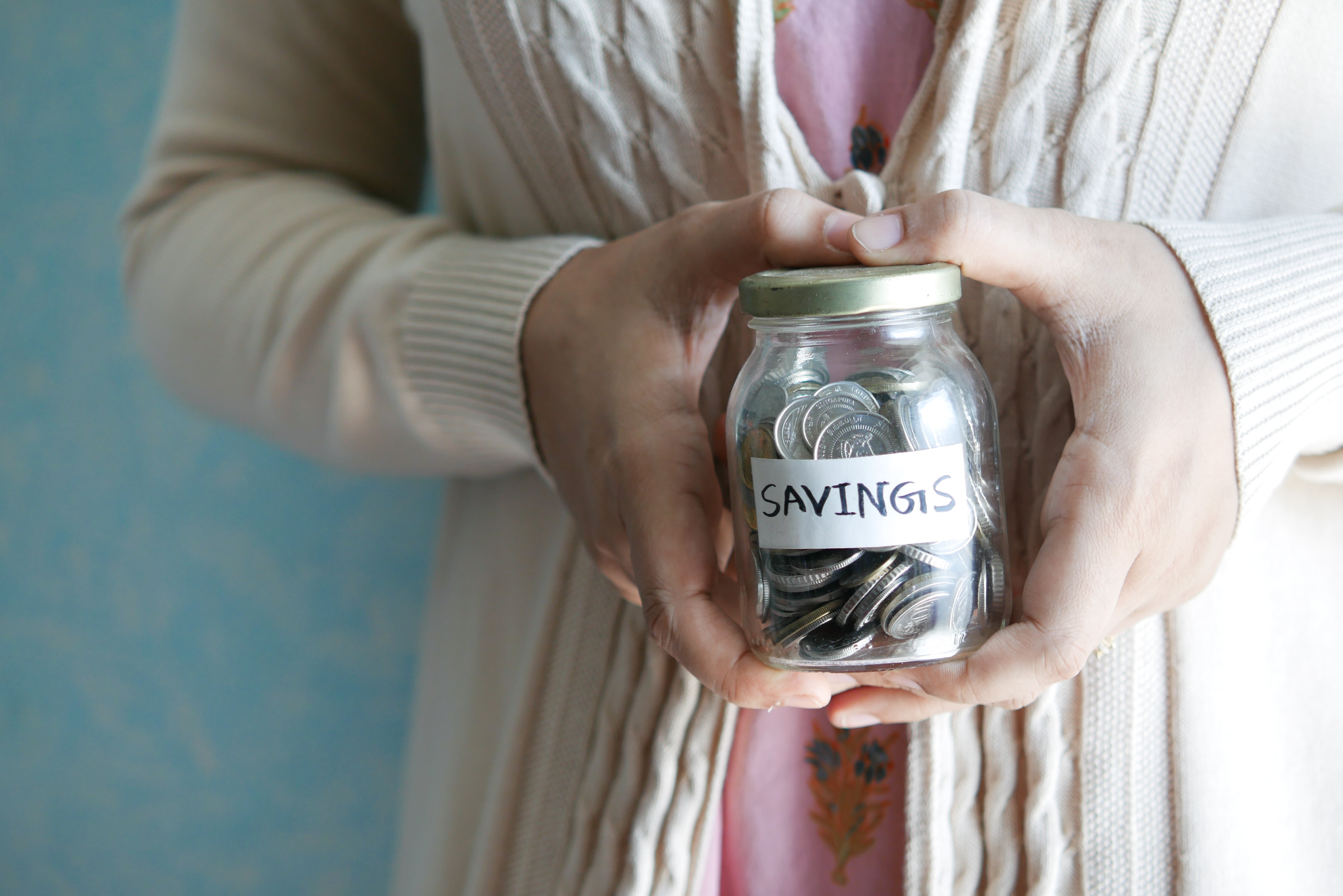 An older person holding a jar of coins labeled "savings."